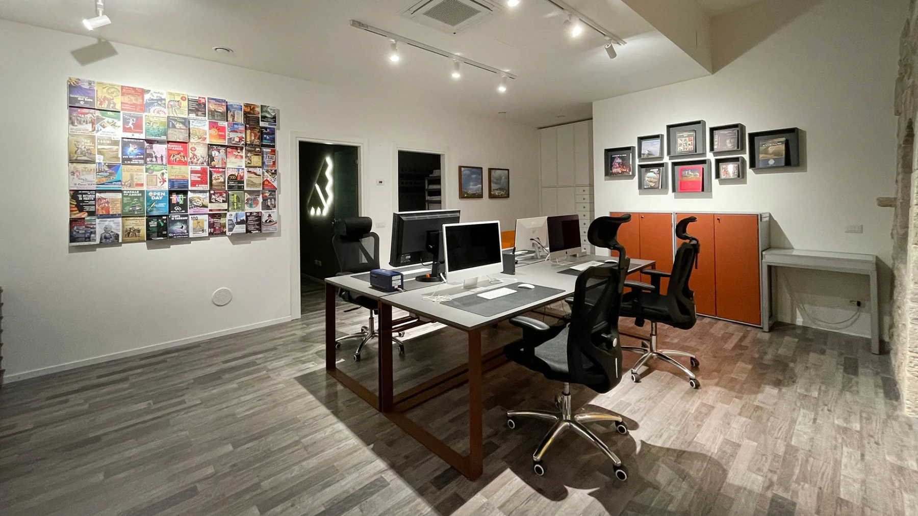 Studio con la parete dei progetti stampati e le postazioni di lavoro